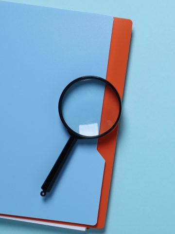 Magnifying glass and notepad on blue background, space for text